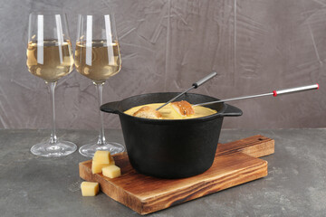 Fondue pot with tasty melted cheese, forks, bread and wine on grey table
