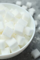 White sugar cubes in bowl on grey table, closeup