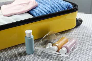 Plastic bag of cosmetic travel kit and suitcase on bed