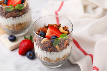 Tasty granola with berries, nuts, yogurt and chia seeds in glasses on white marble table, closeup