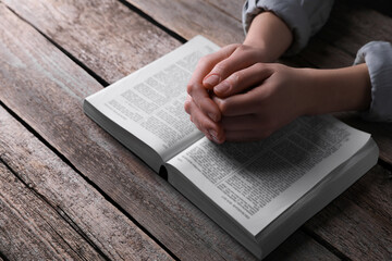 Naklejka premium Religion. Christian woman praying over Bible at wooden table, closeup
