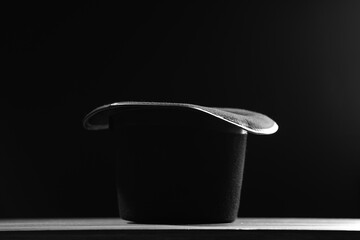 Magician's hat on white wooden table against black background