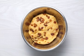 Dough with raisins in bowl on white wooden table, top view