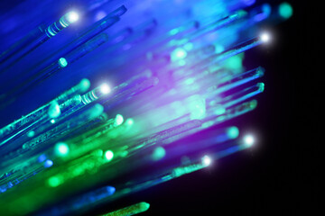 Optical fiber strands transmitting green and blue light on black background, macro view