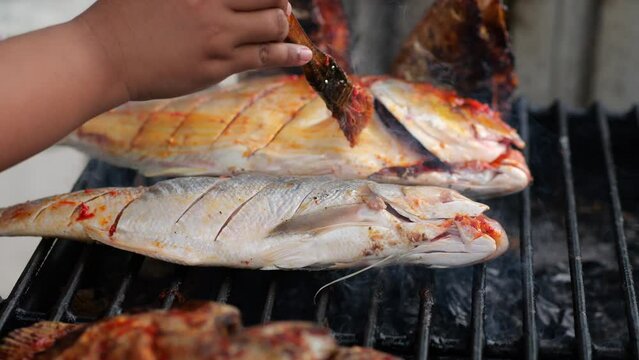 Close-up shot of cooking fish. Baking and roasting marinated fish on barbecue grill. Sea bass or grouper grilled over charcoal. 4K	
