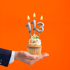 The hand that delivers cupcake with the number 113 candle - Birthday on orange background