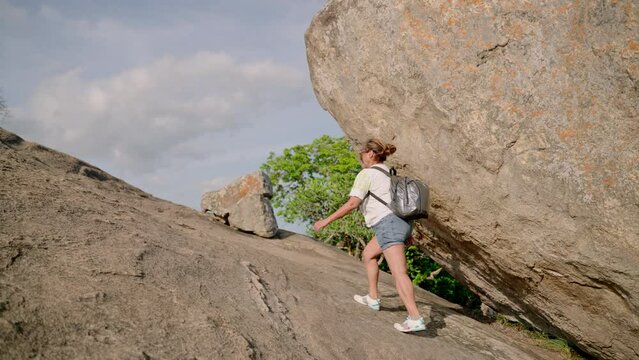 Asian senior woman climbs steep mountain trail with backpack. Elderly hiker conquers Pidurangala Rock, demonstrates vigor in morning hike. Achieves peak, symbolizes perseverance, motivation in nature.