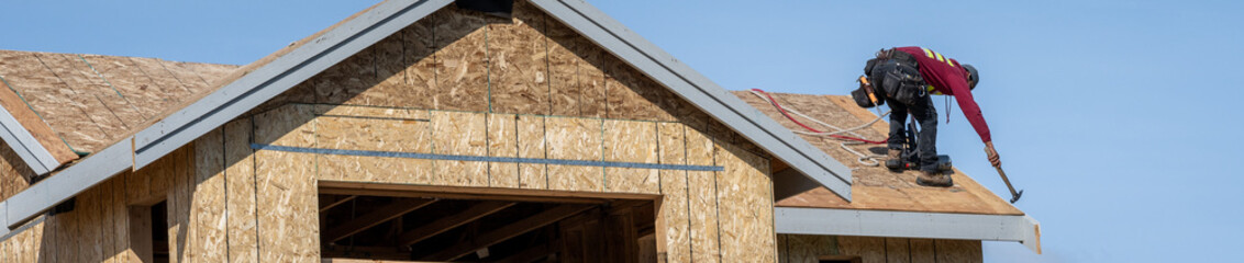 New home construction, minimalist image of new house shell with roofer working on roof, sunny blue sky spring day
