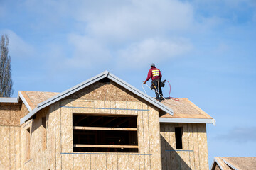 Workman with a nail gun working on roof of new home construction, minimalist image on a sunny...