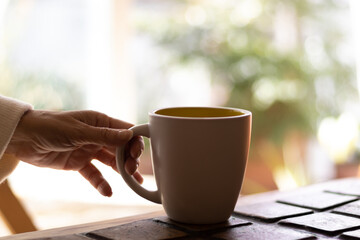 Hand of a mature woman holding a cup of coffee.