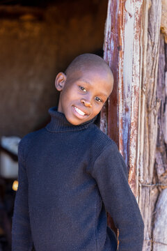 african village, single boy in front of the door outdoors , mud hut interior dirty walls