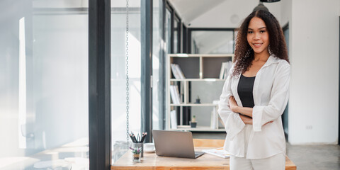 Confident African American businesswoman stands arms crossed in a chic office environment, with her...