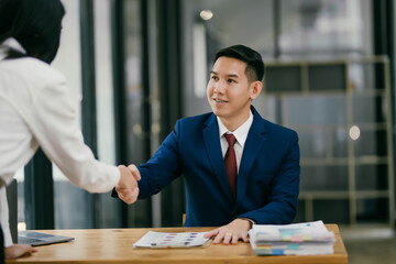 A man in a suit shakes hands with a woman in a white shirt