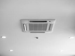 Ceiling mounted cassette type air conditioner decoration near ceiling lights on white building interior. Ceiling type of air conditioning unit with ventilation system.
