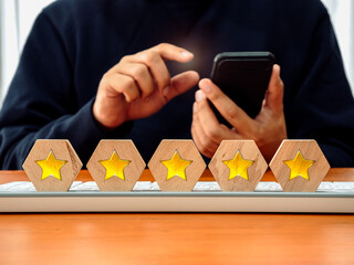 Five star rating, satisfaction, online feedback review service, customer service experience and business marketing evaluation survey. Star symbol on wood block on desk while man using mobile phone.
