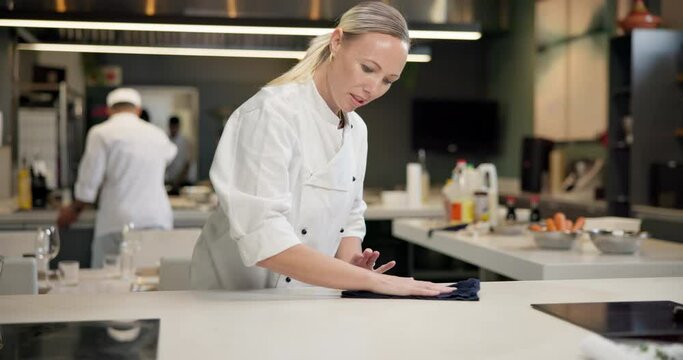 Restaurant, chef and cleaning on table in kitchen for maintenance, food safety and disinfection. Hospitality, compliance and woman with cloth on counter for hygiene, bacteria removal and sanitation