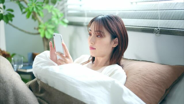ベッドでスマートフォンを見る20代女性