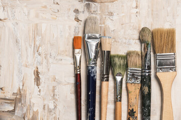 A row of paint brushes on a beige primed canvas background. Artistic creativity concept.Place for text.