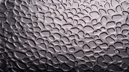 This is a close-up of water droplets on a dark, textured surface. The droplets reflect light, creating a mesmerizing pattern