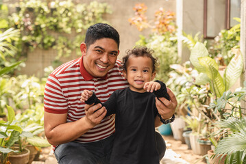 Smiling Asian man enjoys a playful moment with his nephew in a vibrant green garden, showing a heartwarming family bond.