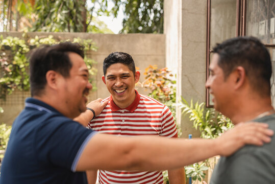 Three asian men recalling their past adventures while outside their home during the summer time.