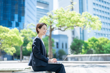 ベンチに座りパソコン作業をする若い日本人女性