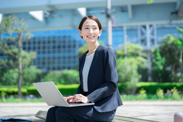 ベンチに座りパソコン作業をする若い日本人女性