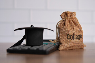 Closeup image of graduation cap, calculator and money bag with word COLLEGE. Financial concept.