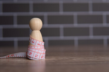 Wooden doll and measuring tape. Diet and weight management concept. Copy space for text.