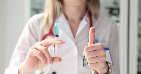 Doctor holds syringe with vaccine or medicine and shows thumbs up