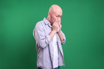 Bald Asian man sneezing in tissue paper isolated on green background