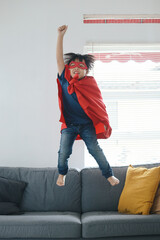Superhero Kid Raising Hand Up and Jump From The Couch As If To Fly, Playing Action Figure at Home.