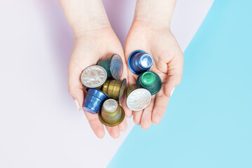Female hands hold capsules for coffee machine on pink and blue background, top view.