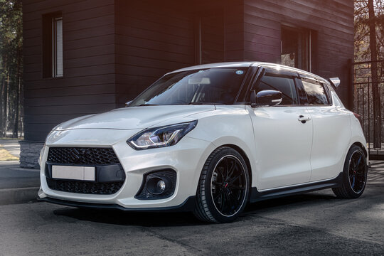 Novosibirsk, Russia - April    23, 2024 :  white Suzuki Swift   ,  front    view,   against  city  in  summer  time