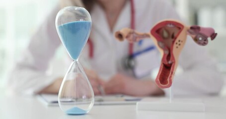 Hourglass and gynecologist with an anatomical model of uterus.