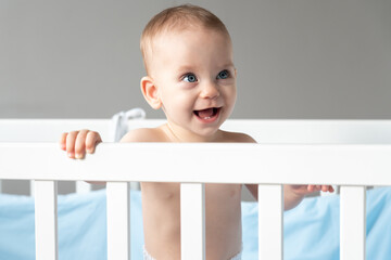 A baby laughing out loud looks out of a crib with interest