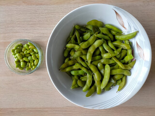Freshly cooked green soybeans in bowls on a light brown wooden surface

