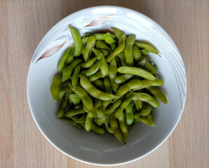 Freshly cooked green soybeans in bowls on a light brown wooden surface
