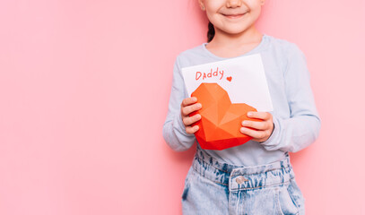 A little girl drew a card for dad on Father's Day in front of a pink background.