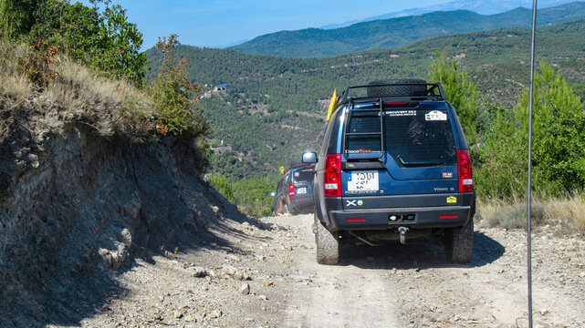 rear view of two blue land rover discovery 3, LR3, prepared for overland trips, going down a hill on a dirt and dust road on an overland trip, in the background you can see the forests of the mountain