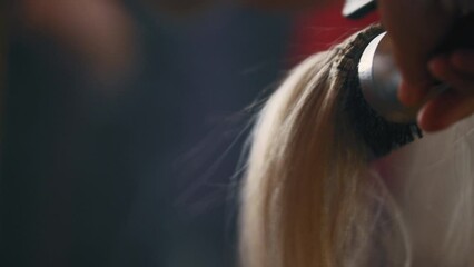 Hair stylist blow drying hair and styling it with a round brush