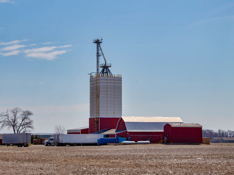 A barn and farm buildings with a square silo for grain storage by a corn field in the countryside.