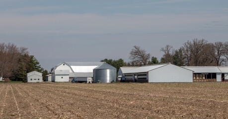 View of farmland and farm buildings. A silo, a farm and a hay factory by a corn field.