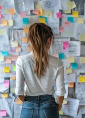 Woman Contemplating a Wall Filled With Colorful Sticky Notes and Documents