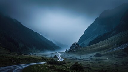 A serene, evening shot of a misty, mountain valley with a single, winding road.
