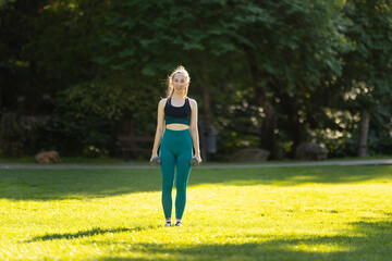 A woman is standing in a park, holding two dumbbells
