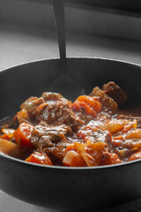 Beef casserole, with herbs and vegetables, in a red wine and tomato sauce. In a black stoneware bowl.