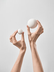 Womans Hands Holding Two Different Sized Spherical Objects Against a Plain Background