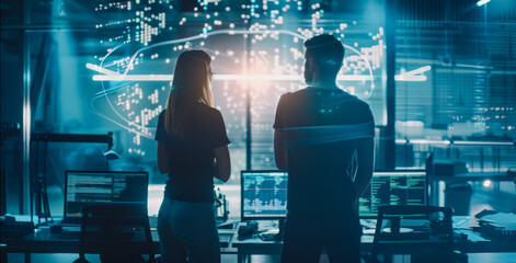 Obraz premium Male and female futuristic IT engineers standing in front of their computers with digital code floating around them