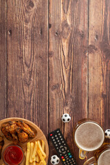 Top vertical view of a wooden table featuring a game day setup with fried chicken wings, French...
